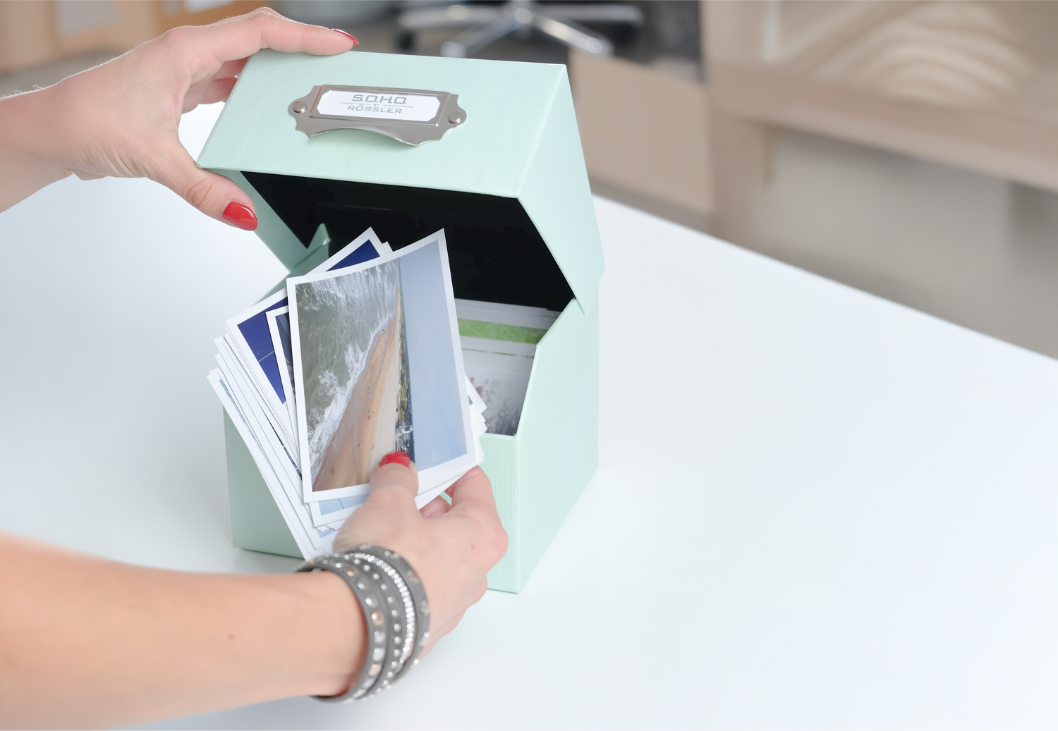 Foto Aufbewahrungsbox mit Metallgriff in der Farbe Mint auf einem Tisch mit Fotos in der Box.